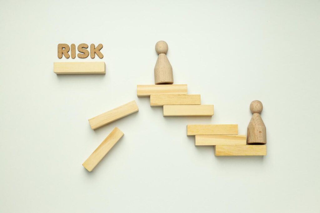 Blocks falling, miniature people models, and the word 'risk'—depicting the potential risks associated with Real Estate Investment Trusts (REITs).